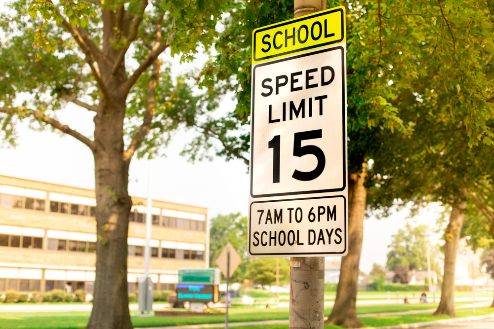 sign indicating school zone speed limit of 15 miles per hour with school building seen in the background